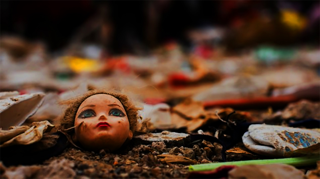 Muñeca rota tirada en el piso en medio de basura